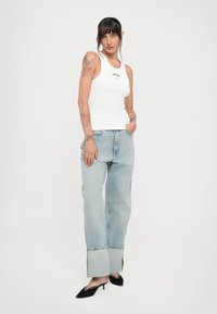Valge sobiv tank top musta logoga, koos helesiniste laia lõikega teksadega, mille alläär on üles keeratud, ja mustade terava ninaga kingadega.