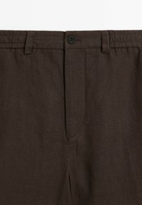 Pantalons en lin marron avec fermeture à bouton, devant plat et poches latérales, finition en tissu texturé.
