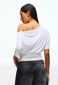 Top bianco scollato sulle spalle con maniche corte, caratterizzato da una vestibilità ampia e tessuto liscio. Abbinato a pantaloni grigio scuro con tasche.