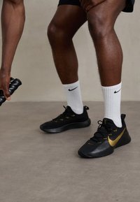 Black athletic shoes with a textured surface, gold accents, and laces, paired with white socks featuring a black logo.