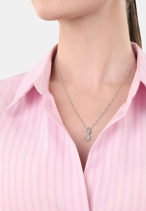 Collar de plata con un diseño de infinito retorcido que presenta un pequeño grupo de rhinestones claros. Llevado sobre una camisa de rayas rosa con cuello.