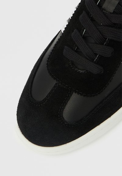 Baskets noires alliant cuir lisse et suède. Design à lacets avec une semelle en caoutchouc blanche et des détails cousus.