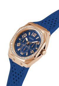Orologio con cinturino in gomma blu, cassa ottagonale in oro rosa, quadrante navy, numeri dorati in grassetto, tre sottodial e accenti in cristallo.