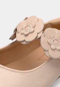 Ballerine en matériau rose doux avec deux appliqués floraux sur le dessus. Bout rond avec bords sans couture et texture lisse.