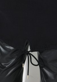 T-shirt nera con orlo curvo e coulisse in vita. Abbinato a pantaloni in finta pelle nera lucida, caratterizzati da una superficie liscia.