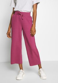 Ribbed, wide-leg pants in a vibrant magenta color with an elastic waistband and drawstring. Styled with a gray t-shirt and white sneakers.