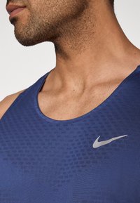 Maiou sportiv bleu marin cu un model texturat, decolteu rotund și un logo Nike argintiu pe partea stângă a pieptului.