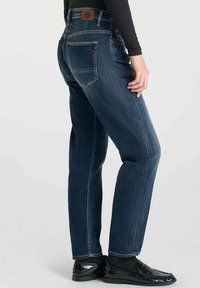 Jeans de mezclilla azul oscuro con corte recto, que cuentan con una etiqueta de cuero marrón en la parte posterior de la cintura y bolsillos traseros con costuras sutiles.