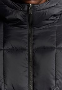 Schwarze Pufferjacke mit durchgehendem Reißverschluss, gestepptem Design mit horizontalen Nähten und hohem Kragen.