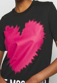 Czarna bawełniana koszulka z krótkim rękawem, z dużym różowym sercem z postarzaną krawędzią; krój z okrągłym dekoltem.