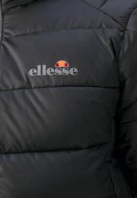 Czarna kurtka puchowa o pikowanej teksturze, z szarym logo "ellesse" oraz wielokolorowym emblematem powyżej.