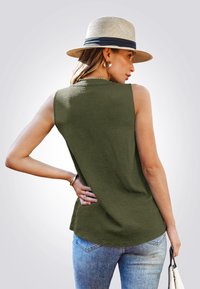 Top sin mangas de color verde oliva con un acabado texturizado, combinado con jeans de color azul claro. La modelo lleva un sombrero de paja y sostiene un bolso.