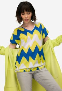 Kortærmet v-hals bluse i blå, gul og hvid zigzag mønster; parret med en limegrøn cardigan; glat stof; afslappet pasform.