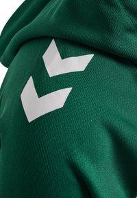 Zielona tkanina o fakturze z dwoma białymi paskami w kształcie szewronów, widoczna w zbliżeniu.