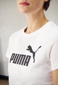 Hvid bomulds t-shirt med et fedt sort "PUMA" logo og en silhuet af en springende puma i sort. Klassisk crew neck design.