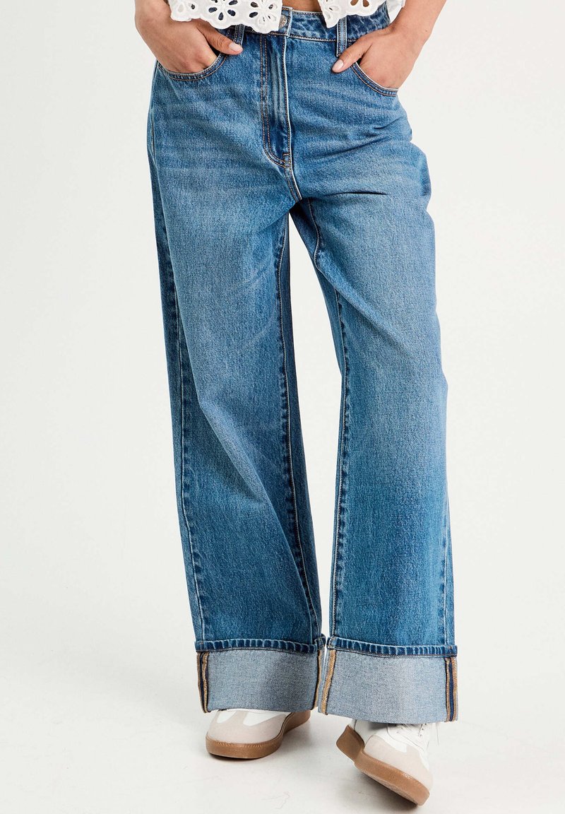 Pantalones vaqueros de pierna ancha en denim, con cintura alta, que presentan dobladillos de puño en contraste y un ligero desgaste a lo largo de las piernas.