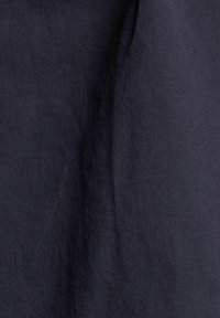 Gros plan sur un tissu bleu marine foncé montrant un tissage sergé diagonal et une couture centrale avec des détails subtils de points.