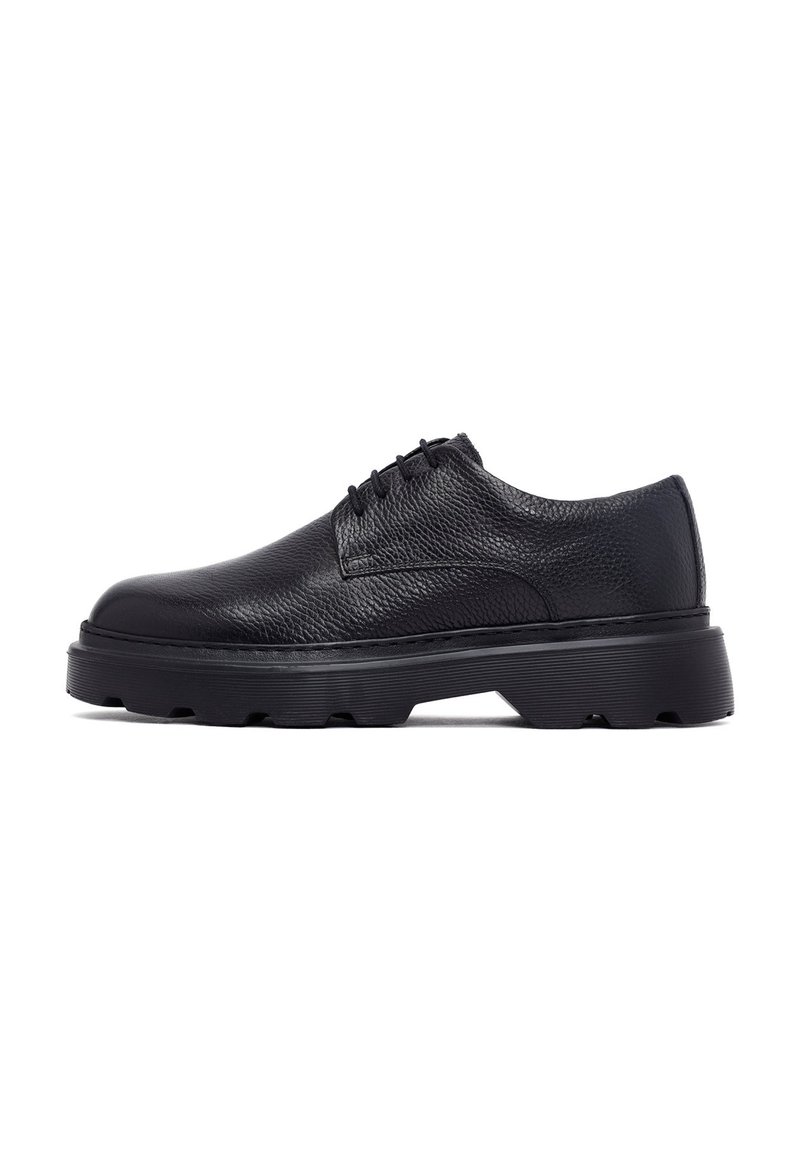 Chaussure oxford en cuir noir avec une finition texturée, bout rond et épaisse semelle en caoutchouc noir dotée d'un motif de semelle rugueux.
