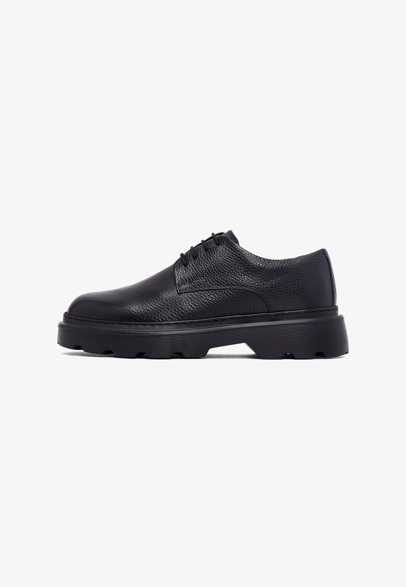 Chaussure oxford en cuir noir avec une finition texturée, bout rond et épaisse semelle en caoutchouc noir dotée d'un motif de semelle rugueux.