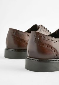 Chaussures habillées en cuir marron avec des perforations décoratives et une finition lisse, dotées d'une semelle en caoutchouc noir robuste pour une meilleure adhérence.