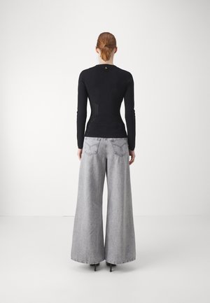 Sort langærmet top med en tætsiddende design og teksturerede detaljer, parret med brede grå denimbukser og sorte højhælede sko.