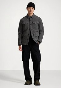 Pilka vilnos ir medvilnės derinimo striukė su sagutėmis, dvi priekinės kišenės, dėvima ant juodos marškinėlių. Derinama su juodomis cargo kelnėmis ir tamsiais sportiniais bateliais.