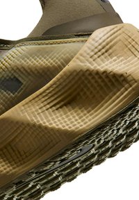 Vihreä ja beige lenkkikenkä, jossa on teksturoitu kumipohja, geometrisia kuvioita ja joustava välipohja. Kenkässä on vahvistettu päällinen ja pehmustettu kantapää.