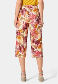 Culottes en tissu crème avec des motifs de feuilles tropicales rouges et orange. La taille est élastique et ils sont coupés juste en dessous du genou.