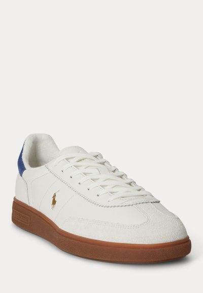 Baskets en cuir blanc avec semelle en caoutchouc marron, languette de talon en daim bleu, lacets blancs et petit logo joueur de polo doré sur le côté.