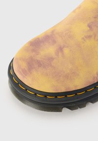 Yellow and purple tie-dye ankle boot with a round toe, contrasting black sole, and yellow stitching on the edge. Textured suede material.