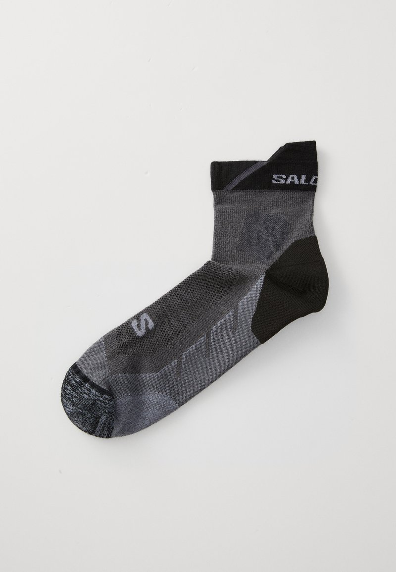 Calcetín gris y negro con un acabado texturizado, puño acanalado, logo en la parte superior y patrones geométricos en los laterales para brindar soporte y transpirabilidad.
