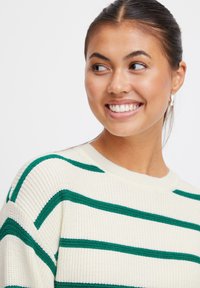 Maglione crema con strisce orizzontali verdi, texture a coste e collo rotondo. Presenta spalle scese e una vestibilità rilassata.