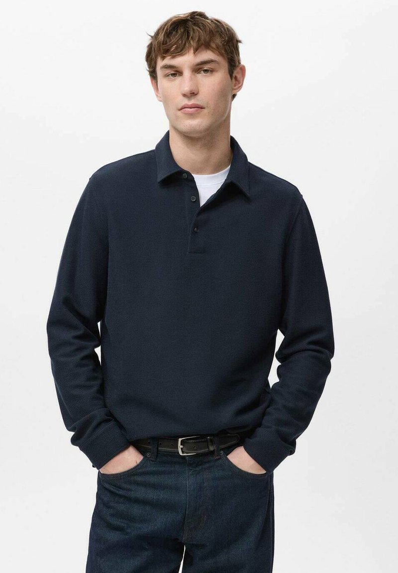 Polo bleu marine à manches longues en tissu texturé avec un col classique, trois boutons et une coupe décontractée, associé à un jean en denim foncé.