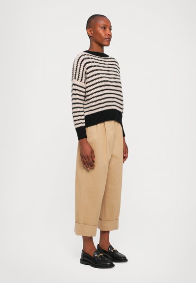 Strikkegenser med svarte og kremfargede striper, oversized passform. Kombinert med beige, løstsittende bukser og svarte loafers. Jevn tekstur.