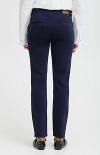Pantaloni in velluto a coste blu navy con una vestibilità dritta, caratterizzati da tasche posteriori e una texture liscia. Abbinati a scarpe nere.