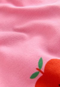 Rosa Stoff mit einer strukturierten, glatten Oberfläche, versehen mit einer Grafik von einer Orange und grünen Blättern in der unteren Ecke.
