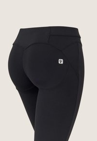 Mustat leggingsit korkealla vyötäröllä, joissa on rakenteellinen malli ja pieni logo takana. Sujuva pinta ja vartalonmyötäinen muoto.