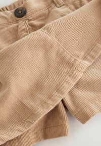 Cordhosen in hellem Beige mit senkrechter Rippung, ausgestattet mit einem dunklen Knopf am Bund und einem umgeschlagenen Saum, der eine weiche Textur zur Geltung bringt.