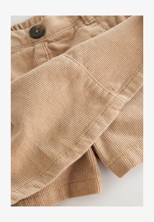 Spodnie kordowe w jasnym beżu z pionowym prążkowaniem, z ciemnym guzikiem w pasie i złożonym dołem, prezentującym miękką teksturę.