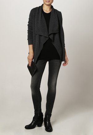 Szary kardigan z miękkiego materiału, z otwartym przodem, zestawiony z czarną bluzką i ciemnymi skinny jeansami. Czarne botki za kostkę dopełniają stylizację.