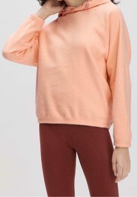 Felpa con cappuccio color pesca in pile con vestibilità comoda, chiusura con coulisse e maniche lunghe. Abbinata a leggings marroni. Texture morbida.