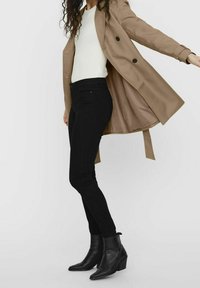 Zwarte skinny jeans gecombineerd met een crèmekleurige ribbeltop en een beige dubbelzijdige jas, met zwarte knopen en een gladde textuur. Zwarte enkellaarsjes maken de look compleet.