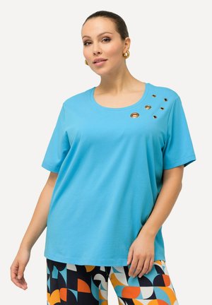 T-shirt in cotone azzurro chiaro con scollo rotondo e occhielli decorativi in bronzo lungo le spalle. Vestibilità ampia con maniche corte.