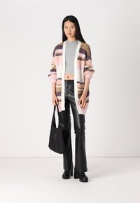 Flerfärgad stickad cardigan med rosa, brun och krämfärgade ränder; kombinerad med en grå croptop och svarta utsvängda byxor; svart toffelväska.