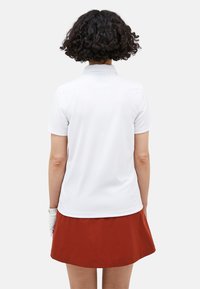 Witte poloshirt met korte mouwen, losse pasvorm en klassieke kraag, gecombineerd met een effen rode rok. Glad materiaal zonder zichtbare patronen.