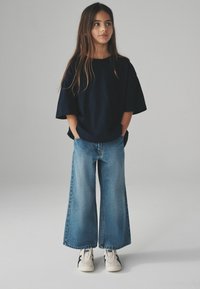 T-shirt navy oversize, jeans light blu con gamba larga e sneaker bianche con accenti navy. I capelli lunghi incorniciano il viso. Outfit semplice e casual.