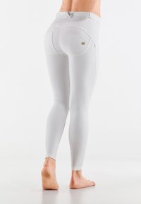 Leggings blancs au design ajusté, avec une taille haute, des poches arrière et de subtils détails de couture. Matériau doux et lisse.