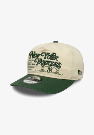 Beige baseballkasket med grøn skygge, med broderet tekst "New York Yankees" og logo. Justerbar størrelse, tekstureret stof på skyggen.