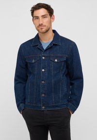 Czarna dżinsowa kurtka z kołnierzykiem, dwoma kieszeniami na piersi, srebrnymi guzikami i dopasowanym krojem. W połączeniu z niebieską koszulką pod spodem.