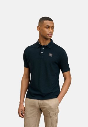 Polo shirt blu navy in cotone misto con scollatura a tre bottoni e patch del logo sul lato sinistro del petto, abbinato a pantaloni cargo beige.